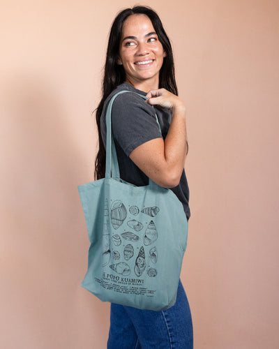 Woman holding a blue-green tote bag with snail shell illustrations on a beige background