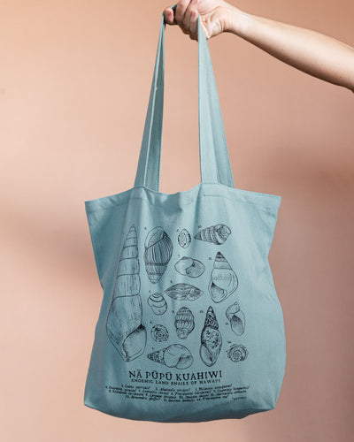 Tote bag with shell illustrations held by a hand against a beige background