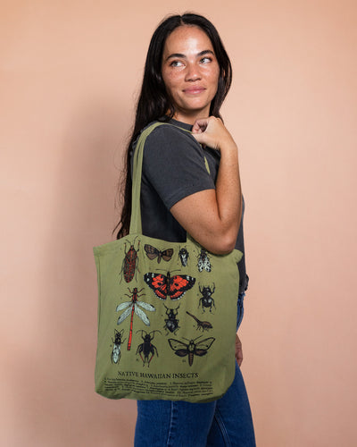 Woman holding a green tote bag with insect illustrations on a beige background