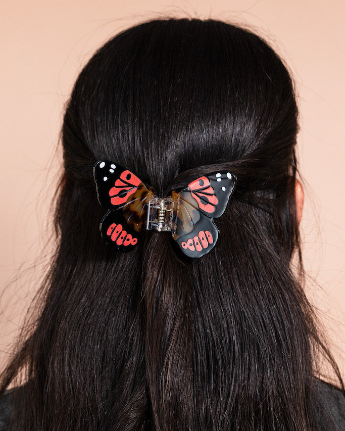 Black, orange, and tortiseshell butterfly hair clip on a person's dark brown hair
