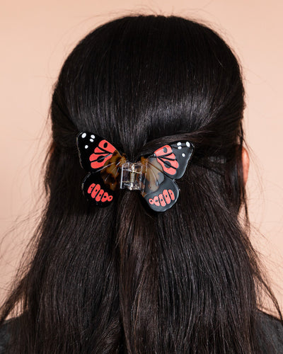 Black, orange, and tortiseshell butterfly hair clip on a person's dark brown hair