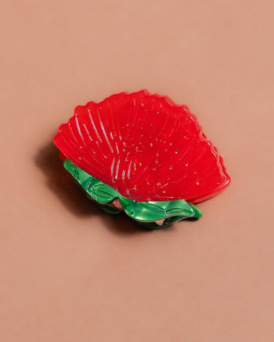 Semi-translucent 'ohi'a blossom shaped hair clip with two green leaves on a beige background