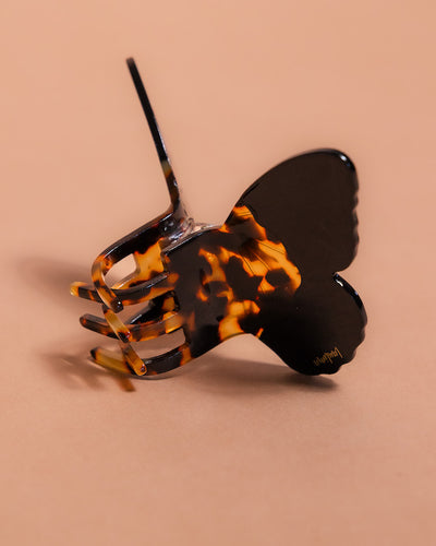 Butterfly-shaped tortoiseshell hair clip rotated to show its teeth against a beige background