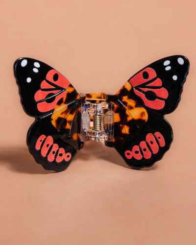 Butterfly-shaped hair clip with tortoiseshell and red accents on a beige background