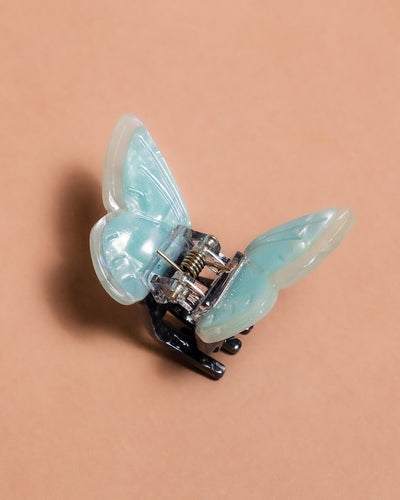 Butterfly-shaped hair clip with semi-pearlescent light blue wings on a beige background
