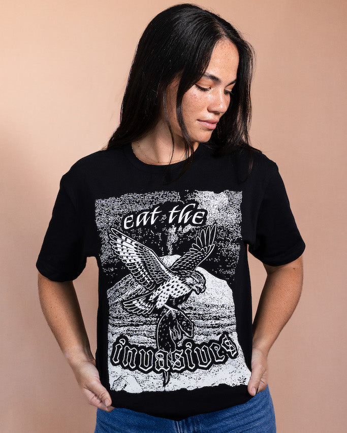 Person wearing a black t-shirt with a white blockprint design of a Hawaiian hawk flying with a mongoose in its claws