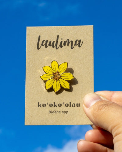 A brown card says Laulima at the top and ko'oko'olau on the bottom, with an enamel pin of a bright yellow flower that has eight petals.